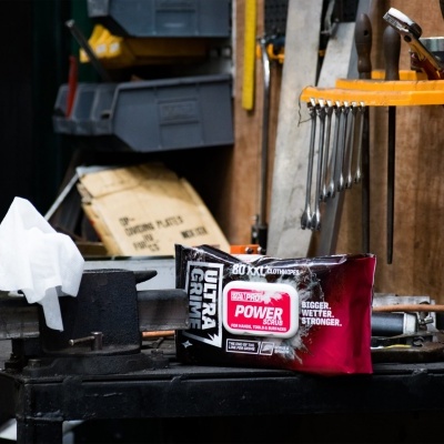 Embalagem vermelha e preta com texto POWER AUTOTERRA sobre bancada de oficina com ferramentas e morsa.