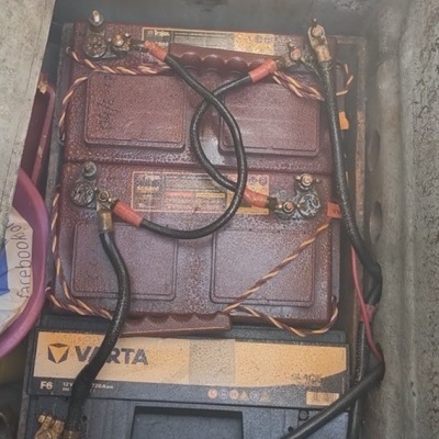Duas baterias de automóvel VARTA com cabos ligados numa caixa metálica suja