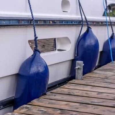 Defensas azuis amarradas a um barco branco no cais de madeira