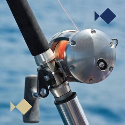 Carreto metálico prateado em vara de pesca com linha laranja e água ao fundo