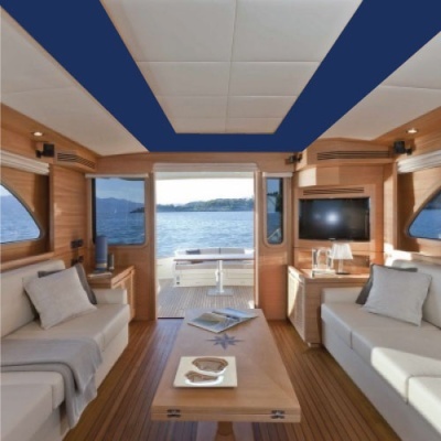 Interior de iate com sofás brancos, mesa de madeira, janelas para o mar e televisão