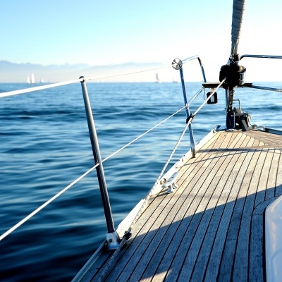 Convés de veleiro com piso de madeira e corrimão metálico no mar