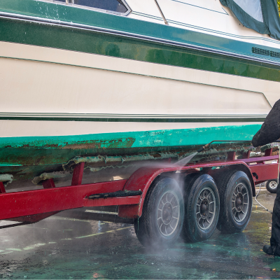 Barco branco com faixa verde escura sendo limpo por pessoa com roupa preta em reboque vermelho de três eixos