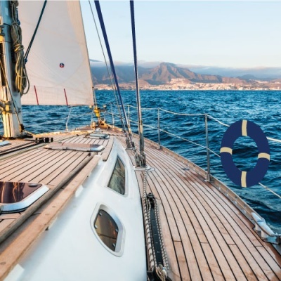 Convés de iate em madeira clara com vela branca e mar ao fundo