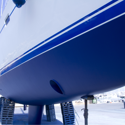 Parte inferior do casco de um barco azul e branco apoiado em suportes num estaleiro náutico