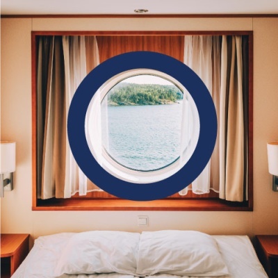 Janela redonda azul com vista para água e ilha em quarto com cama branca e cortinas castanhas e brancas