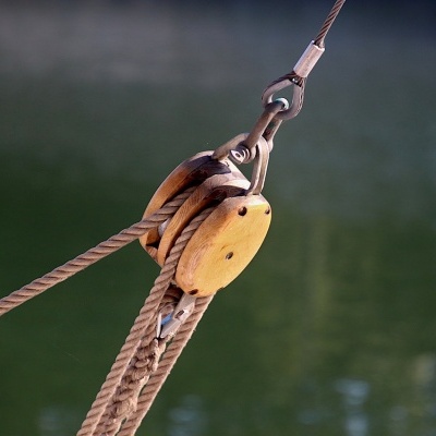 Roldana náutica de madeira com cordas e cabo de aço sobre água