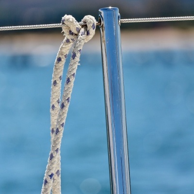 Corda branca com padrões azuis amarrada a cabo de aço e barra metálica com mar ao fundo