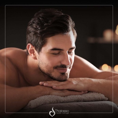 Homem deitado de bruços sobre toalha cinzenta num ambiente interno com luz suave