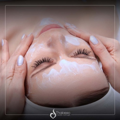 Mulher a receber massagem facial com produto branco e mãos de terapeuta