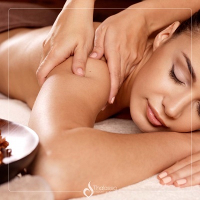 Mulher a receber massagem nos ombros, de olhos fechados, deitada numa toalha branca