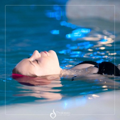 Mulher a flutuar numa piscina interior com fato de banho preto e faixa rosa