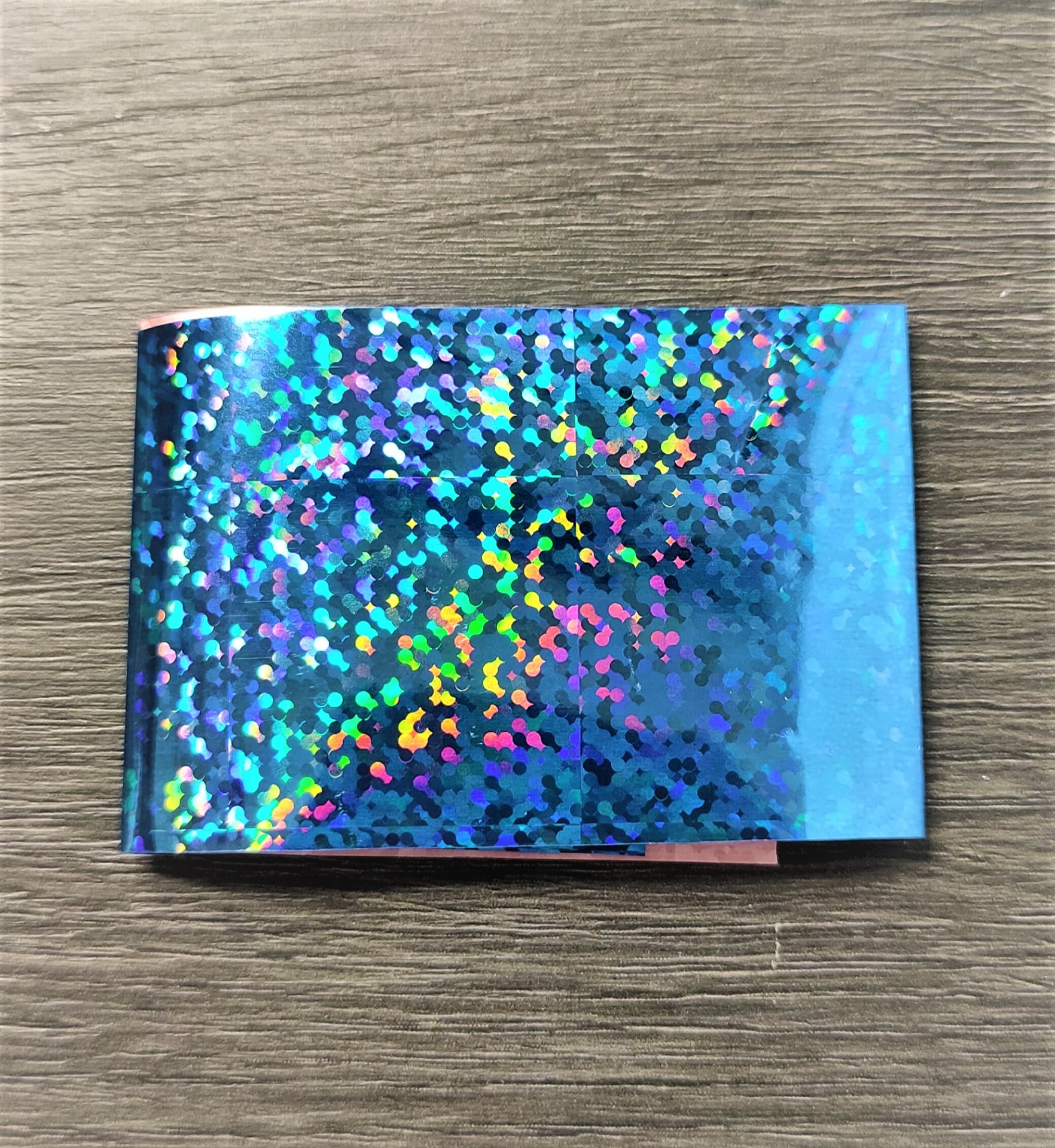 Folha autocolante holográfica azul com padrão brilhante sobre madeira cinzenta
