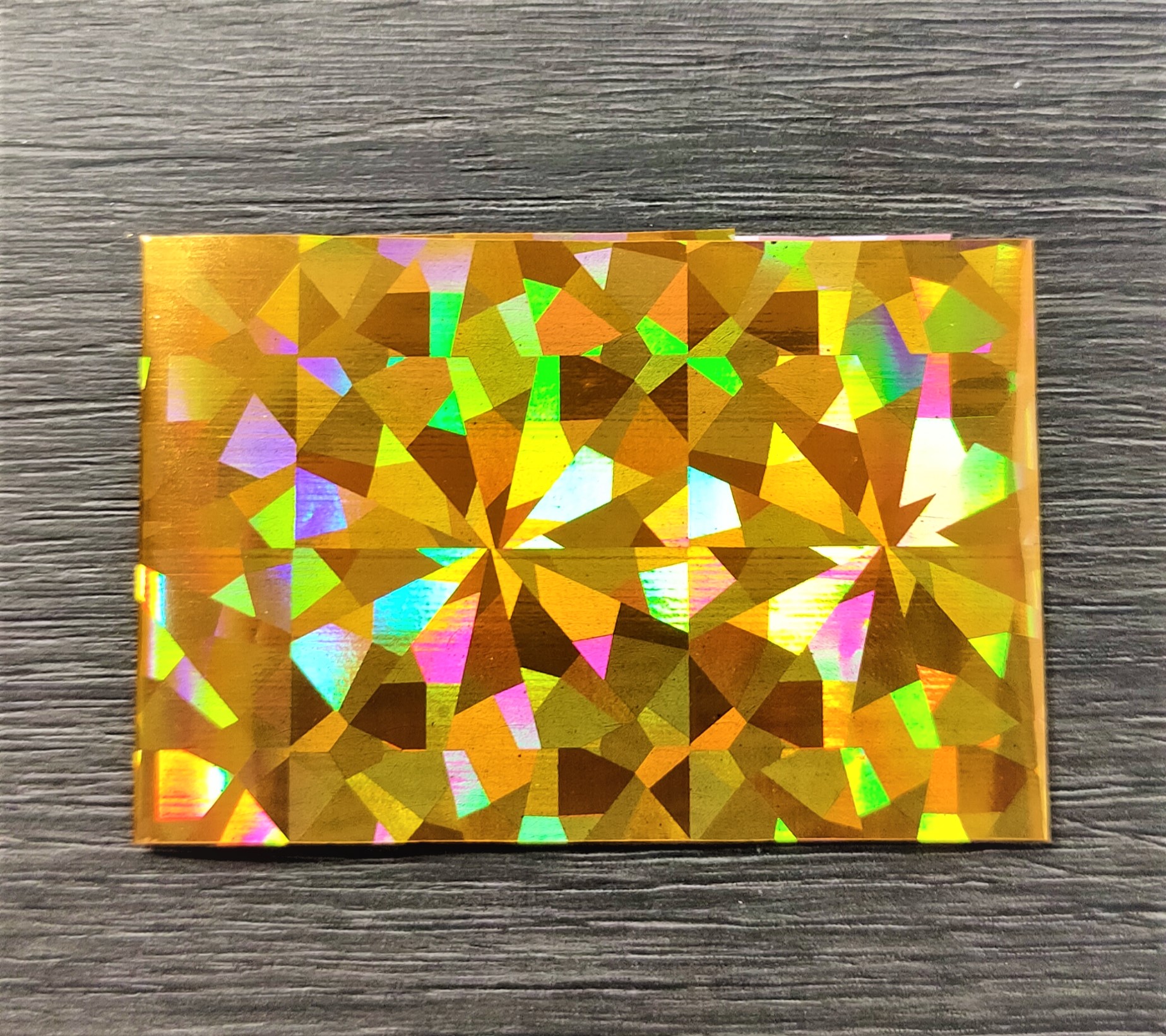 Cartão holográfico dourado com padrão facetado sobre madeira escura