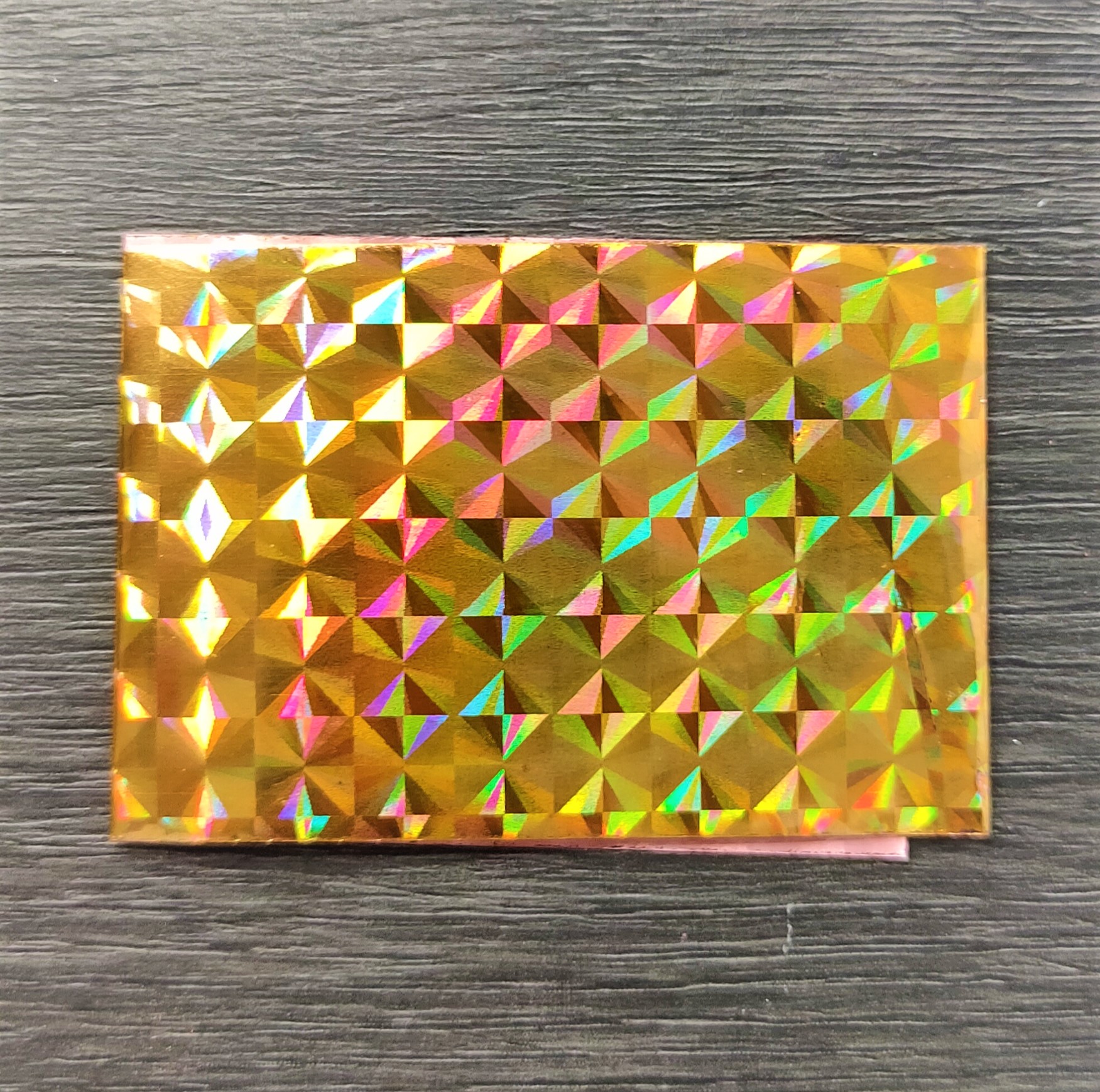Envelope holográfico dourado com padrão geométrico sobre superfície cinza