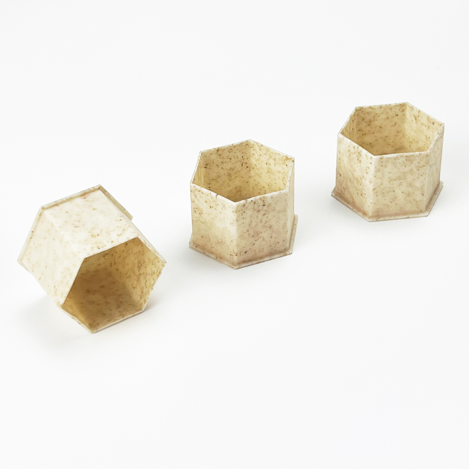 Três recipientes hexagonais bege com textura sobre fundo branco