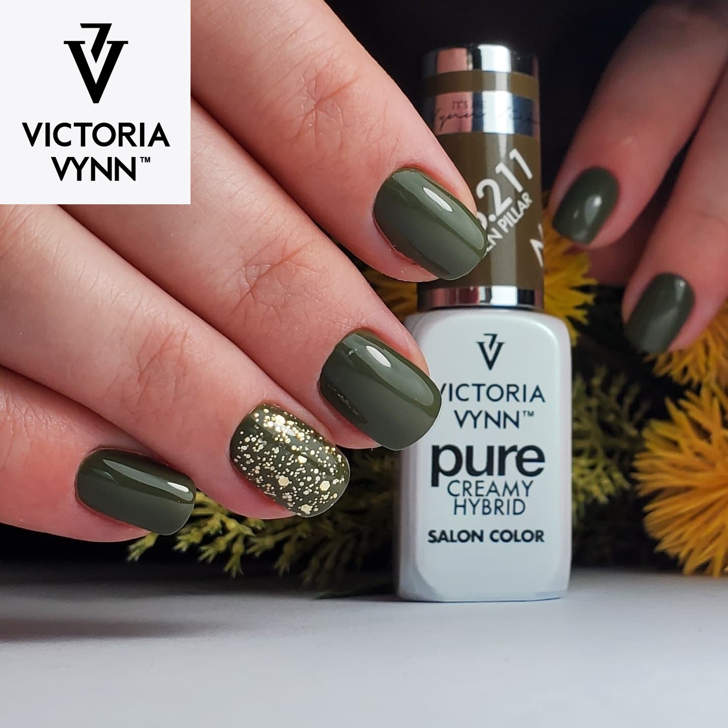 Unhas pintadas de verde escuro com anelar dourado segurando frasco de verniz Victoria Vynn