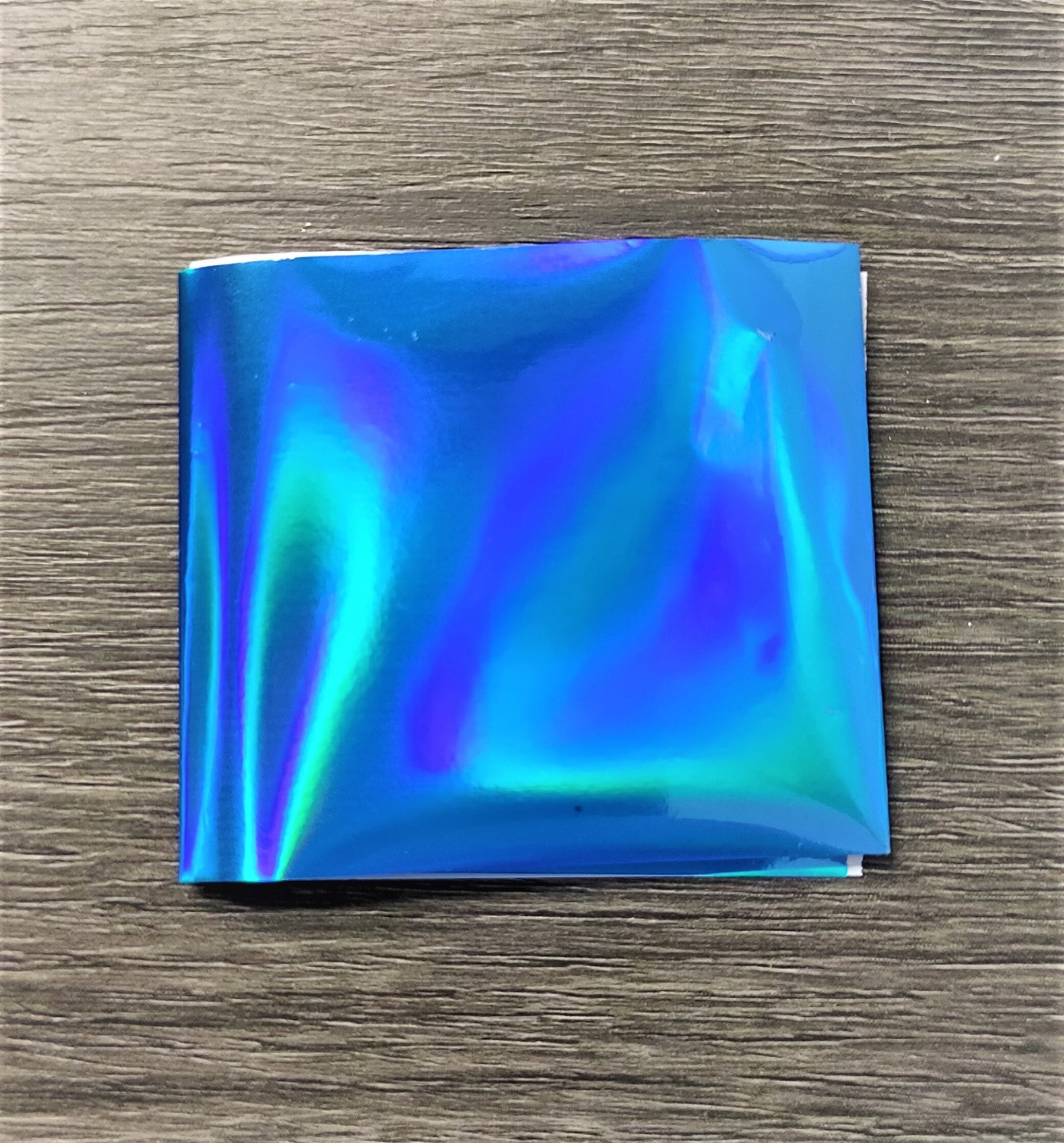 Folha metálica azul iridescente sobre superfície de madeira escura