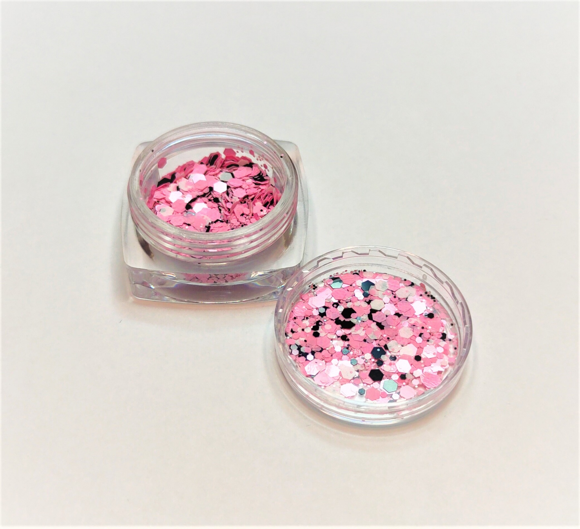 Frasco pequeno com purpurina rosa e branca com tampa ao lado sobre fundo claro
