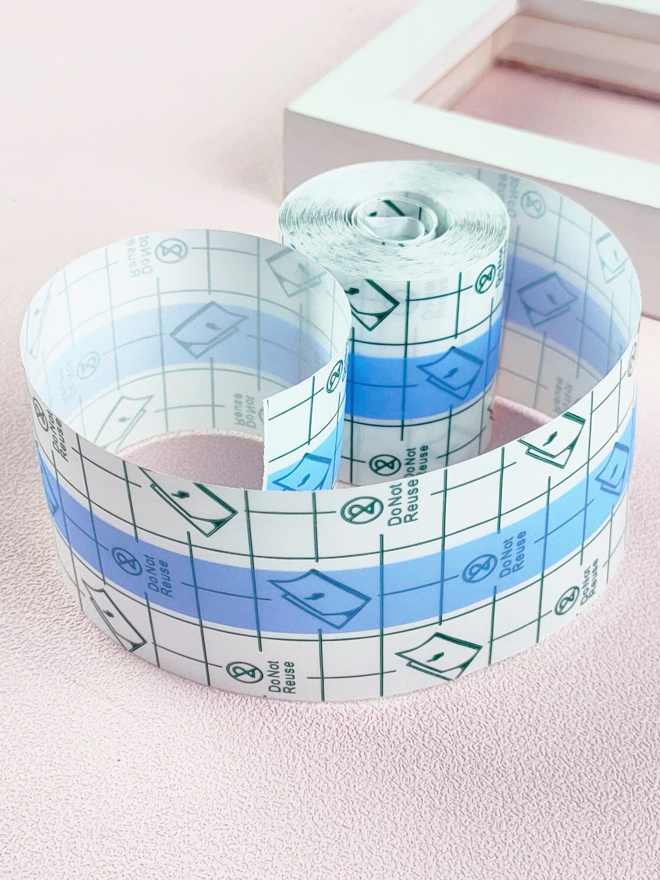 Rolo de fita adesiva transparente com padrões e texto, sobre superfície rosa