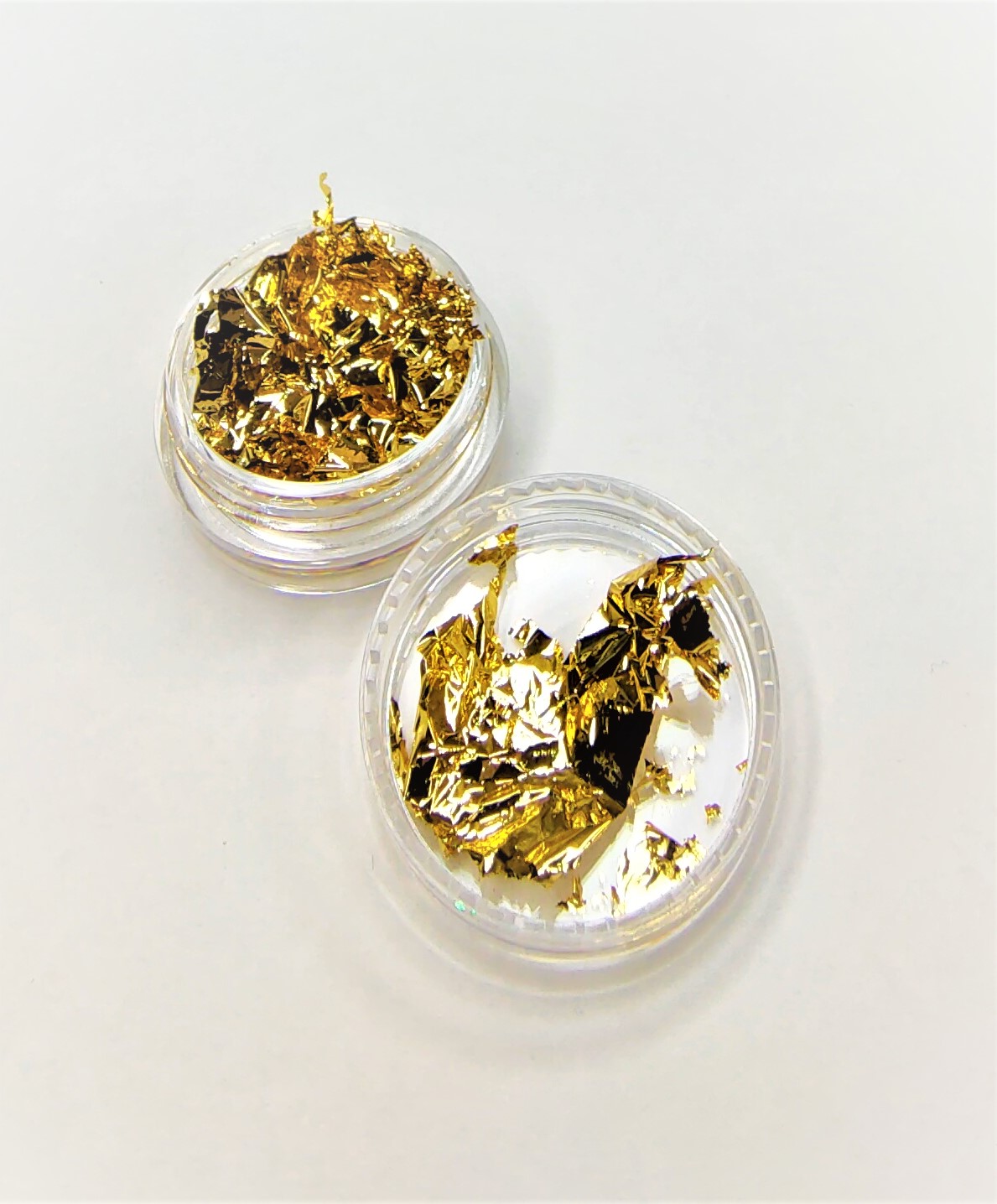 Folhas douradas finas em embalagens circulares transparentes sobre fundo branco