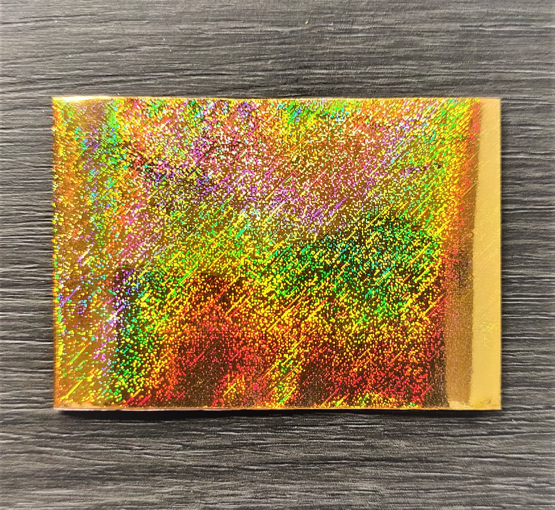 Cartão holográfico colorido sobre superfície de madeira cinza escuro.