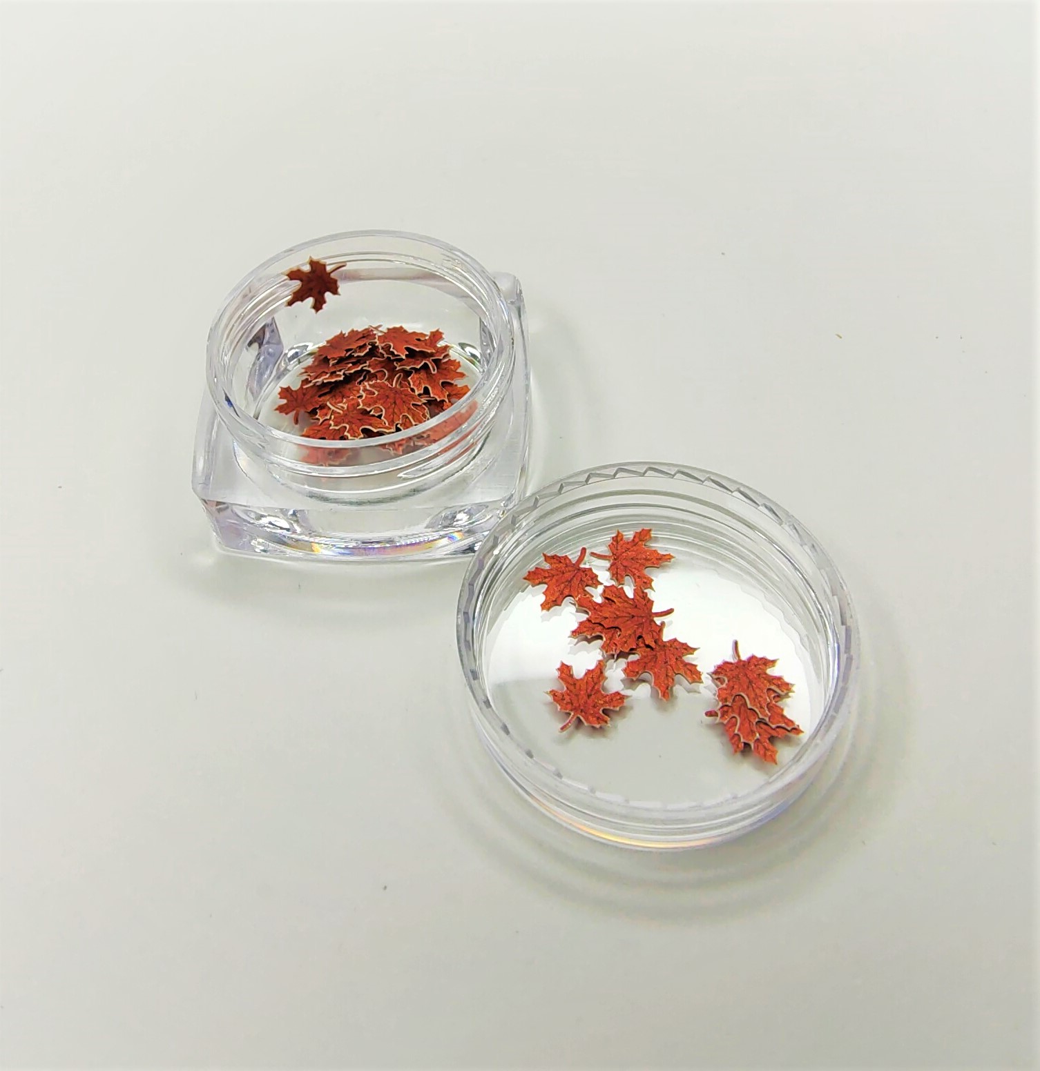 Frascos transparentes com folhas vermelhas decorativas em forma de bordo sobre fundo branco