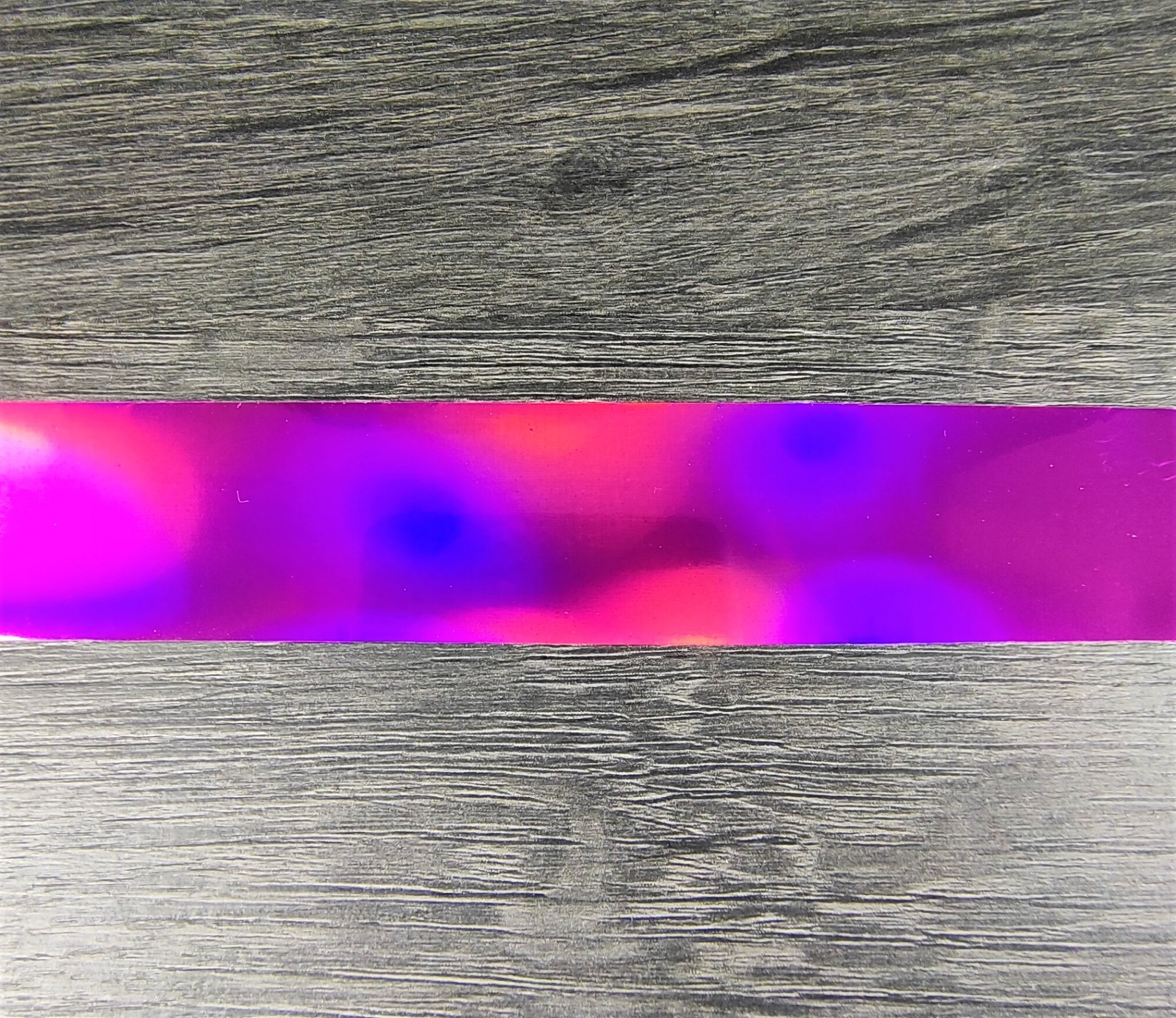 Fita plástica holográfica rosa e roxa sobre superfície cinza imitando madeira