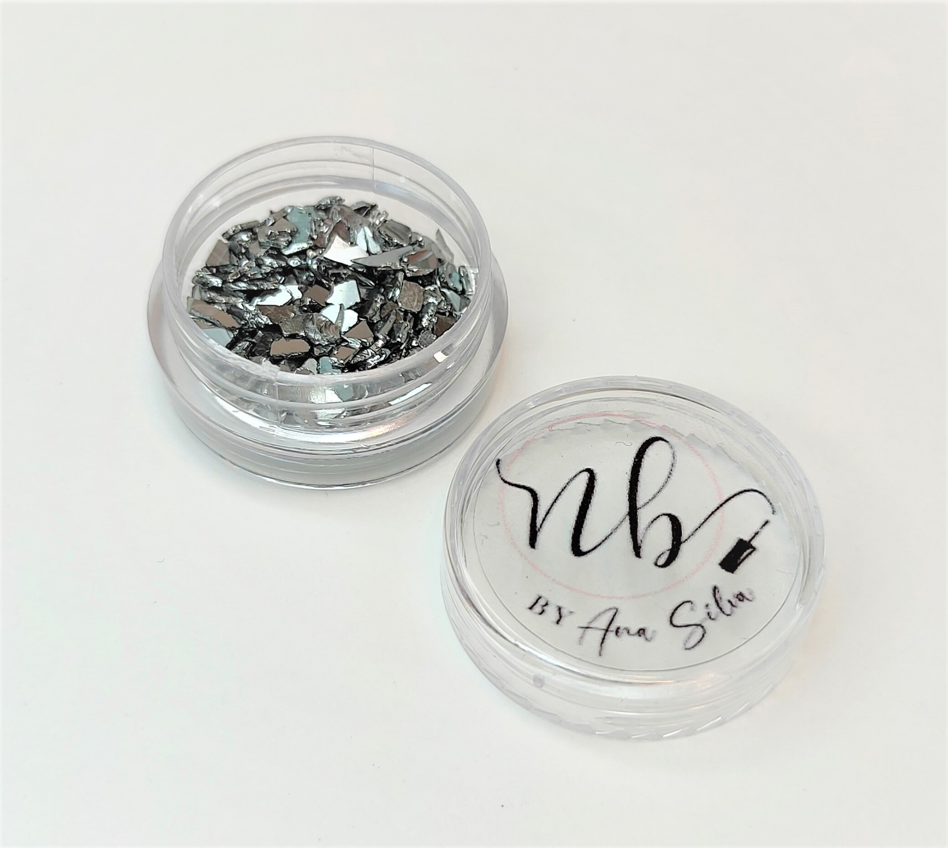 Embalagem transparente com pequenas peças prateadas e texto 'nbv By Ana Silva'