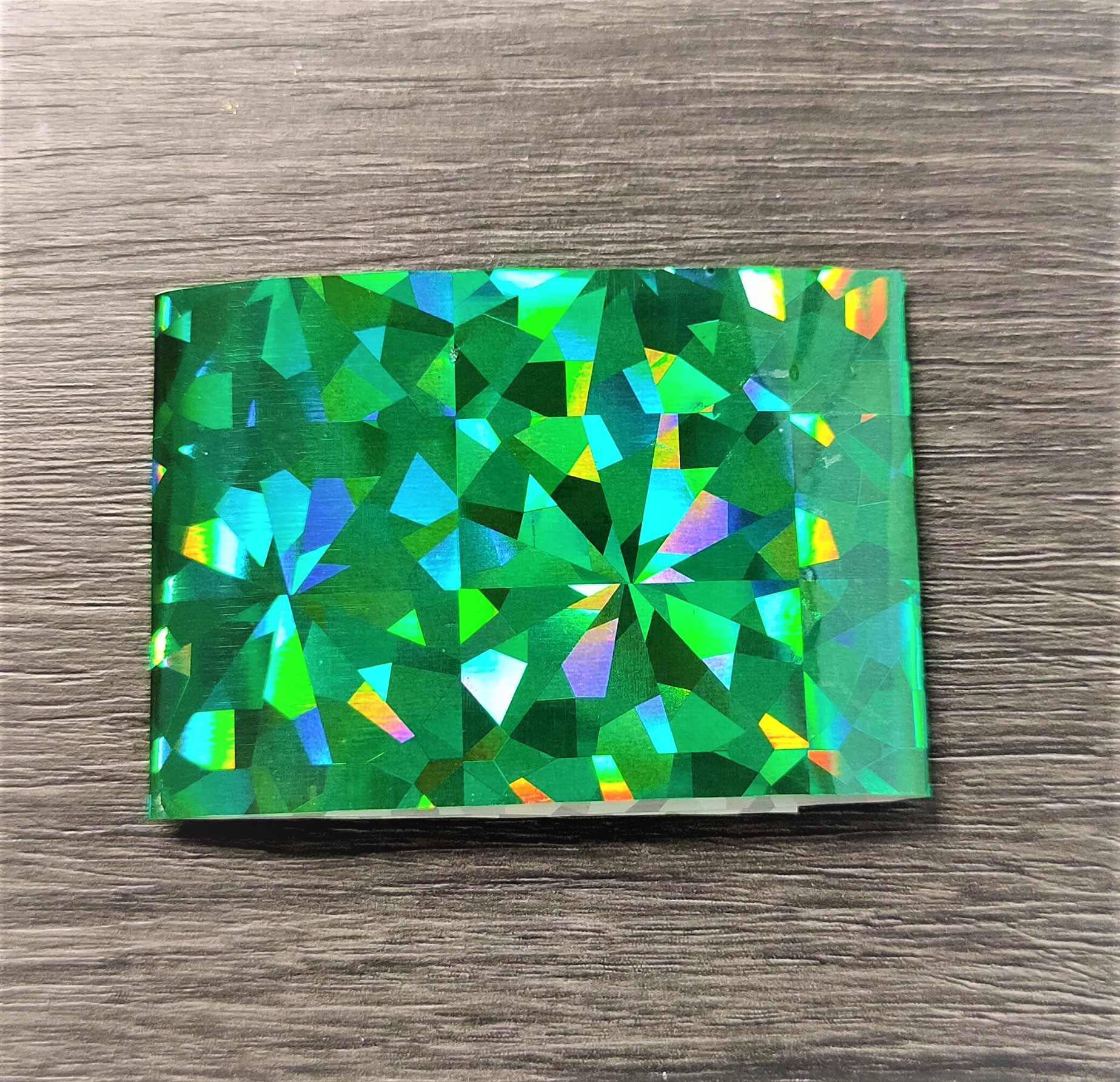 Película holográfica verde com padrão geométrico sobre superfície de madeira