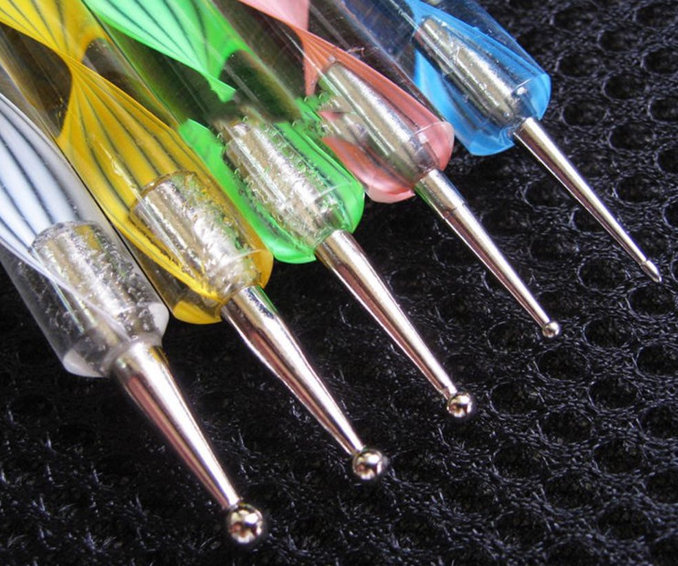 Ferramentas coloridas para decoração de unhas com pontas metálicas sobre fundo preto