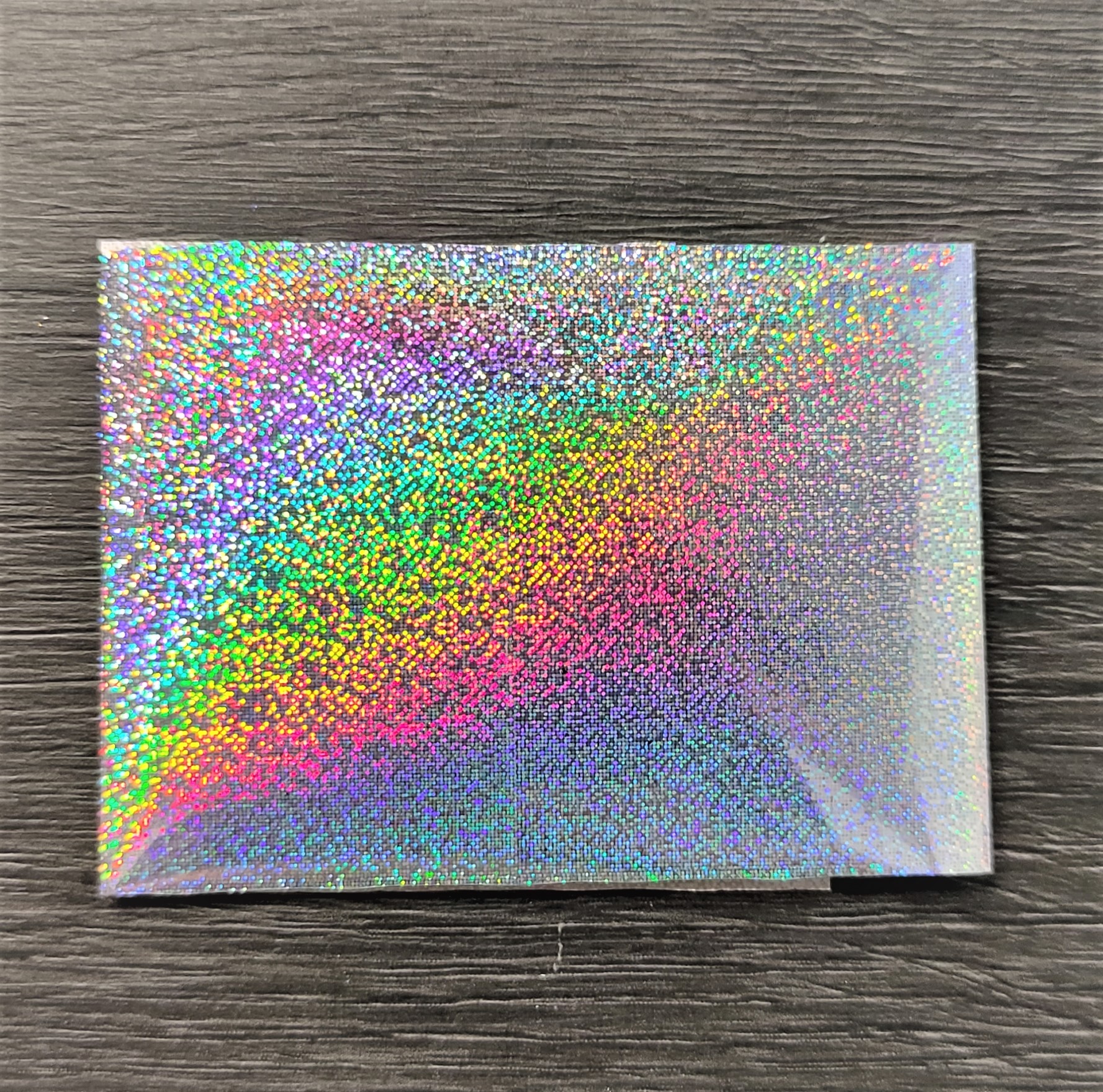 Caixa holográfica prateada com reflexos coloridos sobre madeira escura