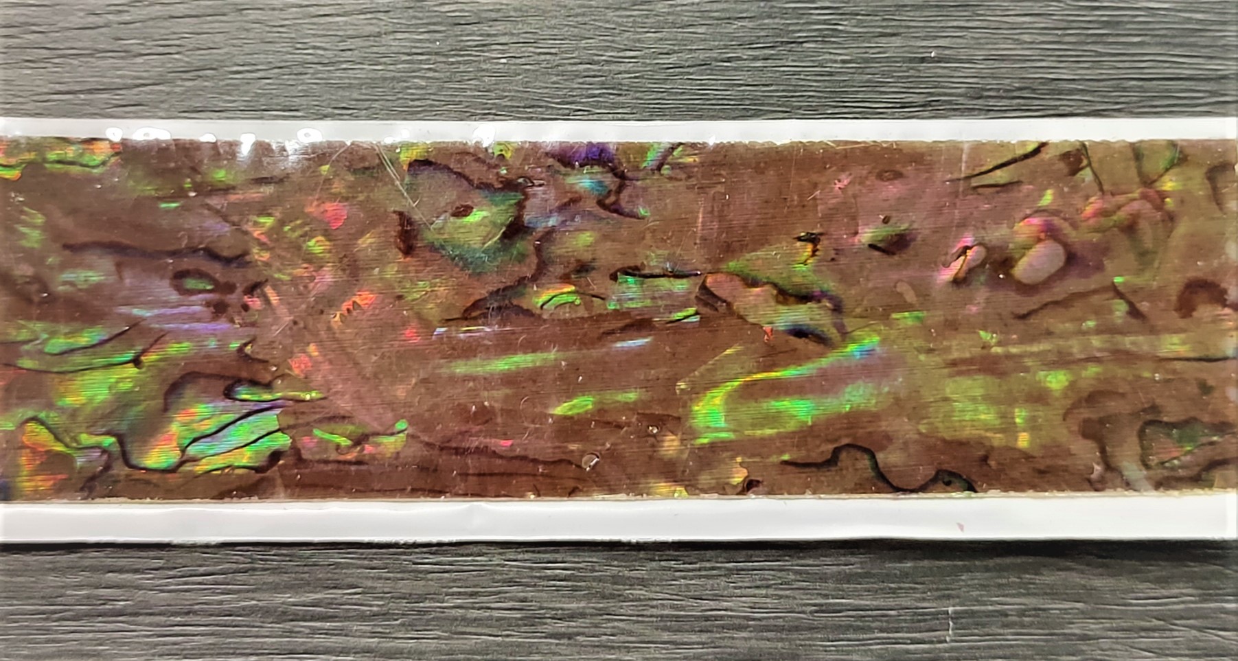 Fita adesiva decorativa com padrão iridescente e relevo sobre madeira cinzenta