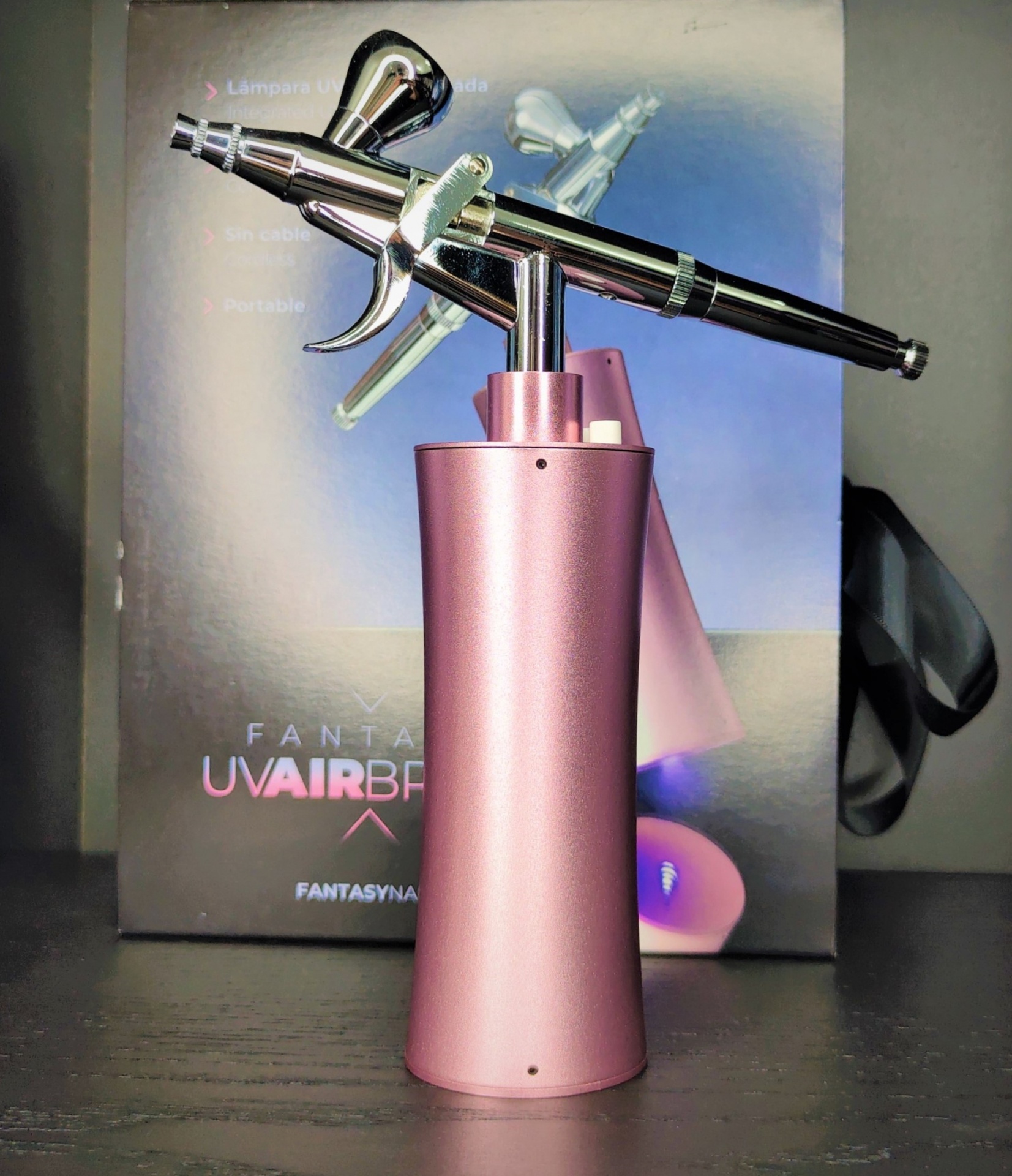 Aerógrafo metálico com base rosa diante de caixa com texto UV AIRBRUSH