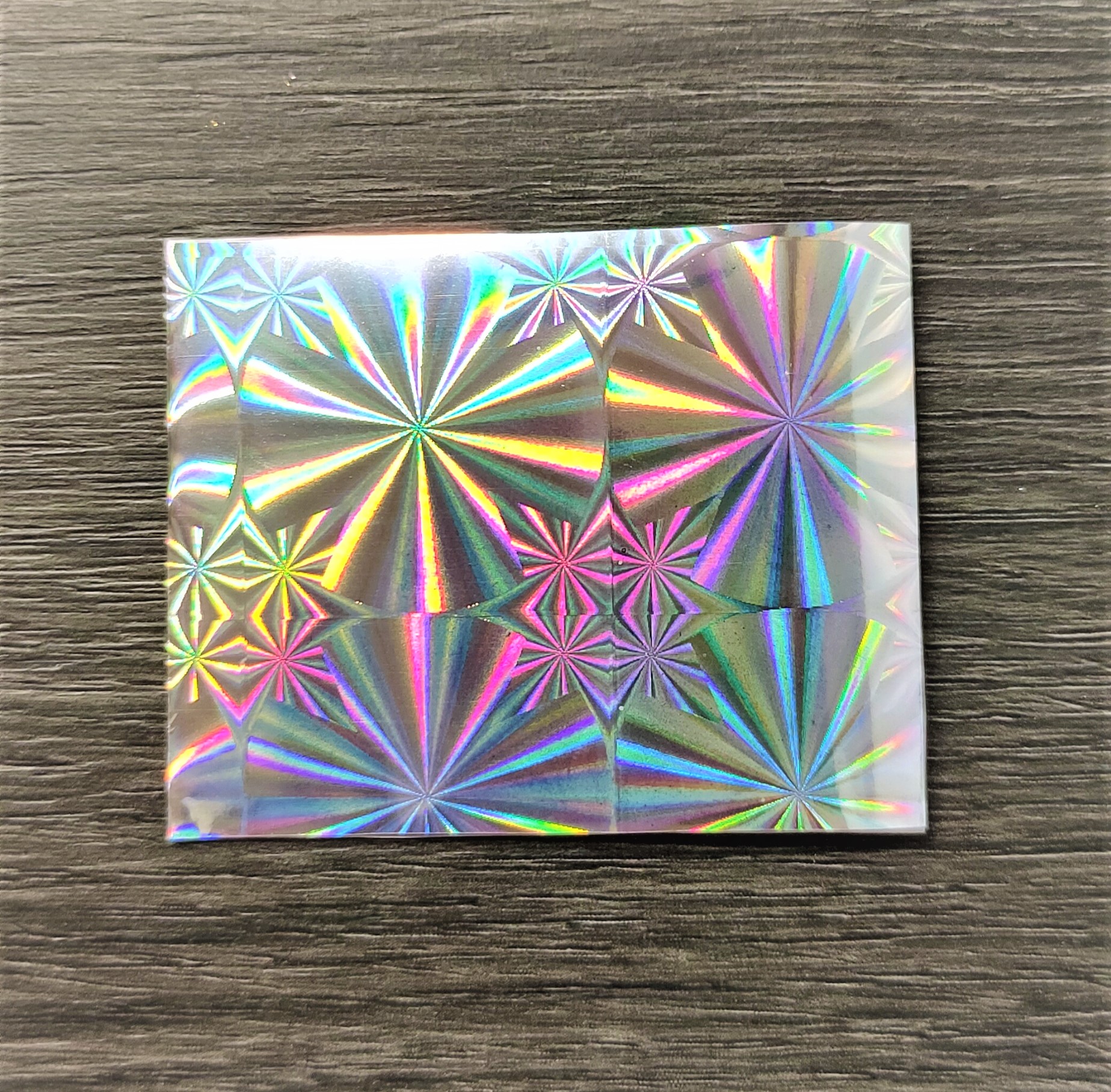 Papel holográfico com padrão de estrelas e círculos coloridos sobre fundo cinza