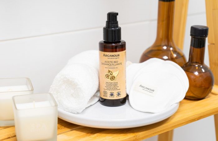 Frasco de cosmético Arganour com toalhas e discos de algodão em prateleira de madeira