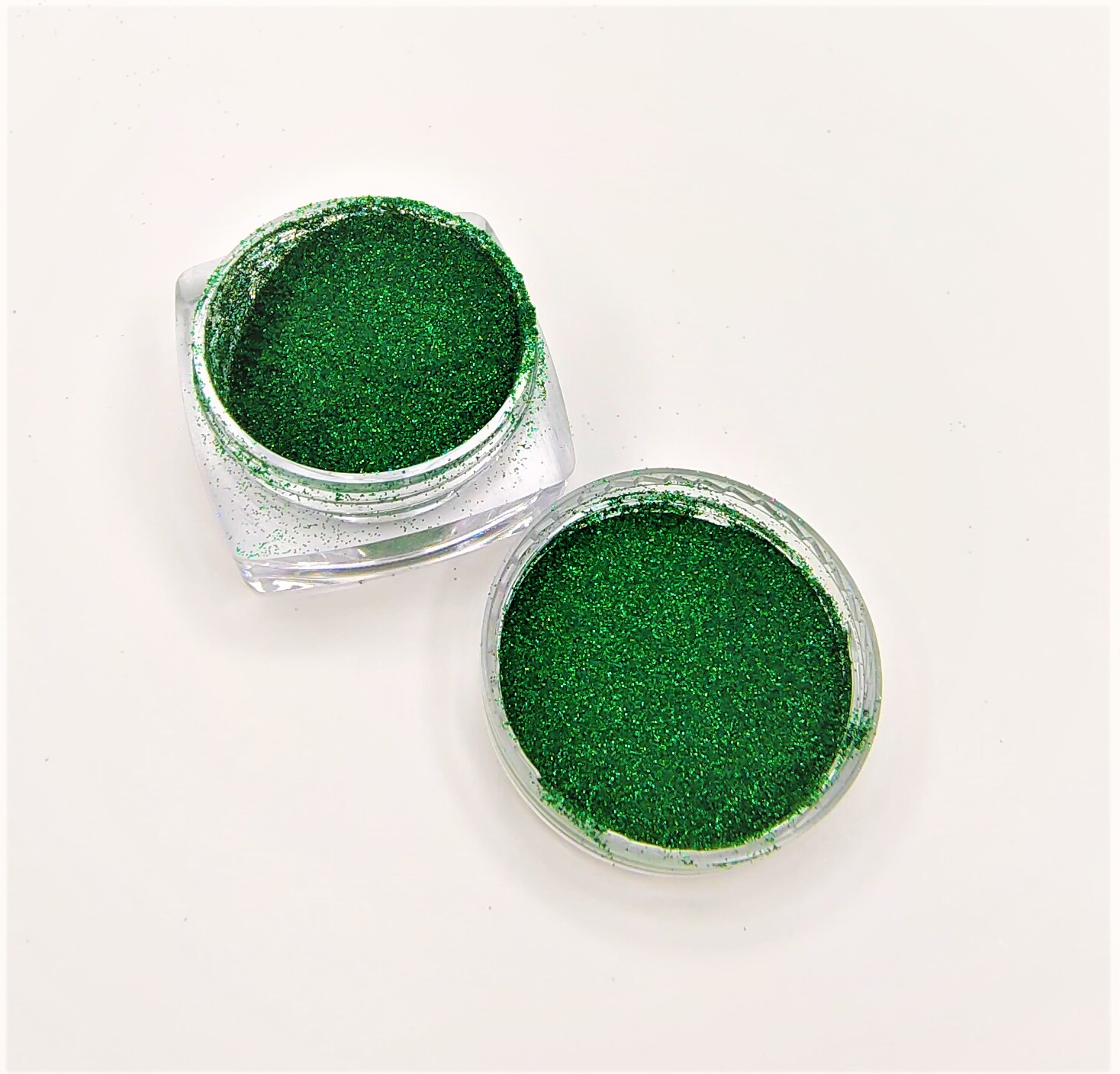 Dois recipientes com glitter verde, um aberto e outro com tampa ao lado, sobre fundo branco.