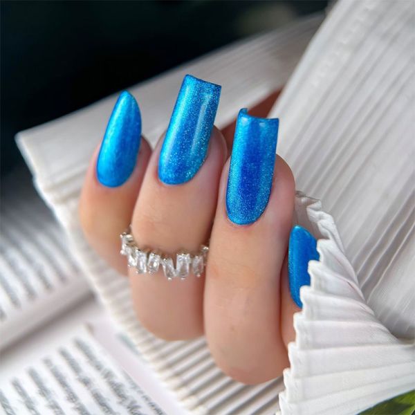 Unhas compridas com verniz azul metálico em mão com anel prateado e manga branca