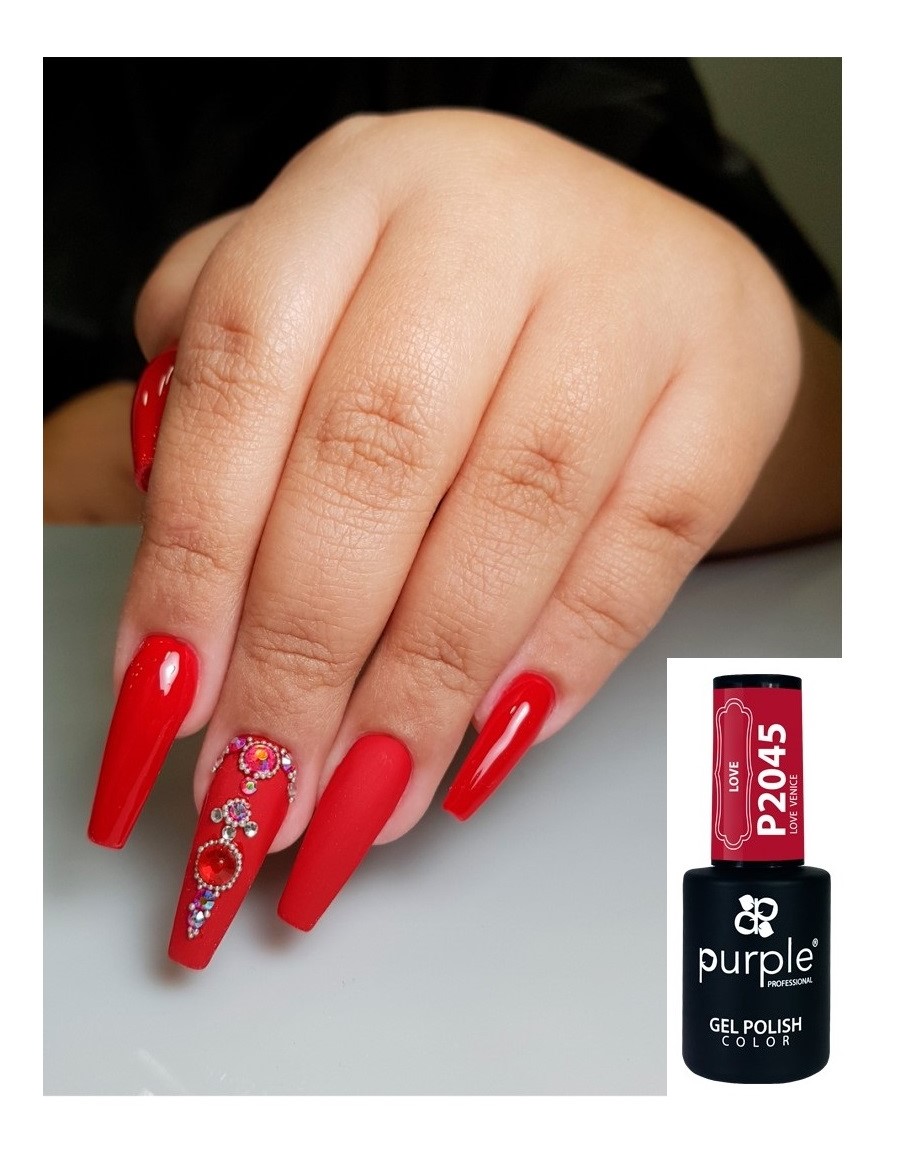 Mãos com unhas vermelhas foscas decoradas com pedras e frasco de verniz gel vermelho.