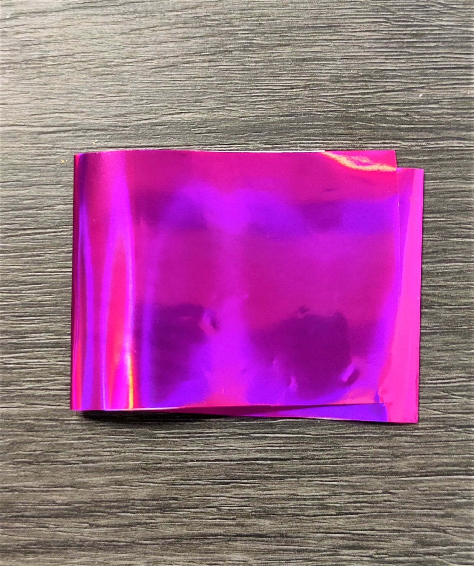 Folha de material plástico metálico rosa com efeito iridescente sobre superfície de madeira cinza