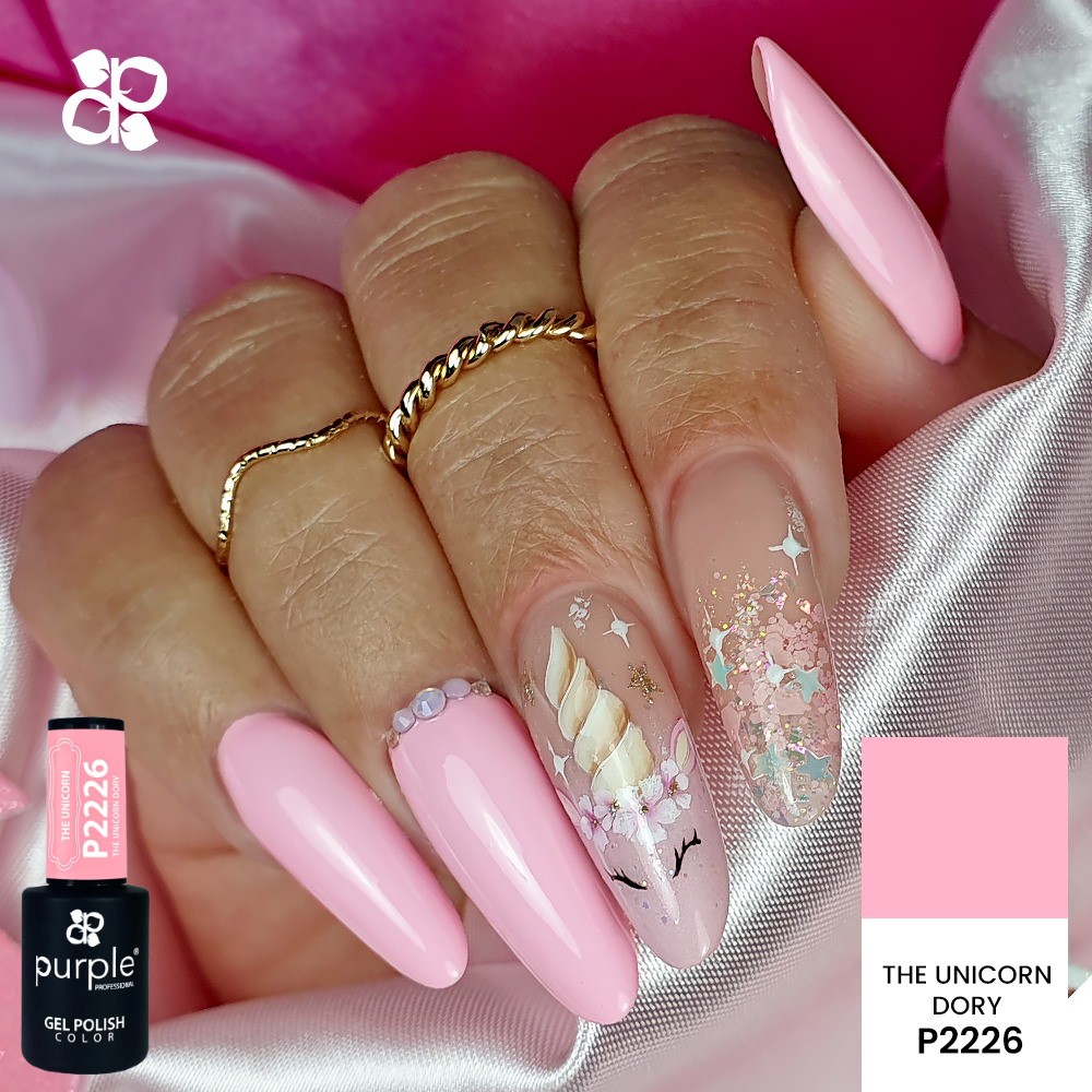 Unhas rosas decoradas com glitter e desenho de unicórnio, com anéis dourados finos nos dedos