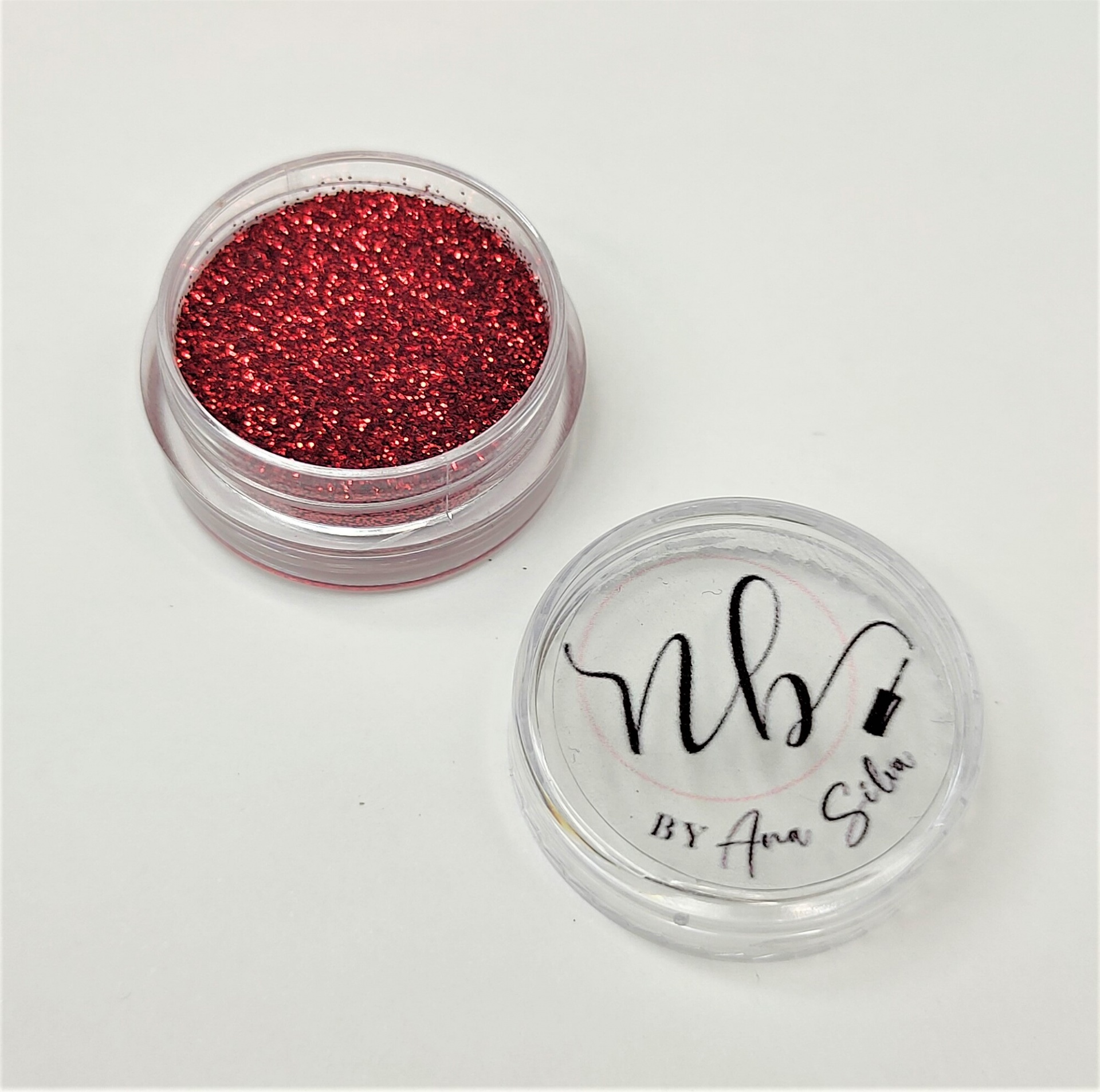 Pote redondo transparente com glitter vermelho e tampa com texto 'nb BY Ana Silva'