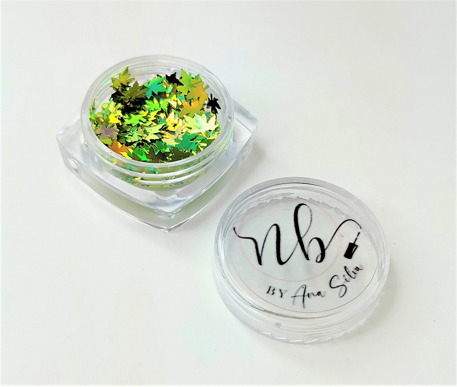 Frasco pequeno com purpurina em forma de folhas verdes e douradas e tampa com texto nb BY Ana Silva