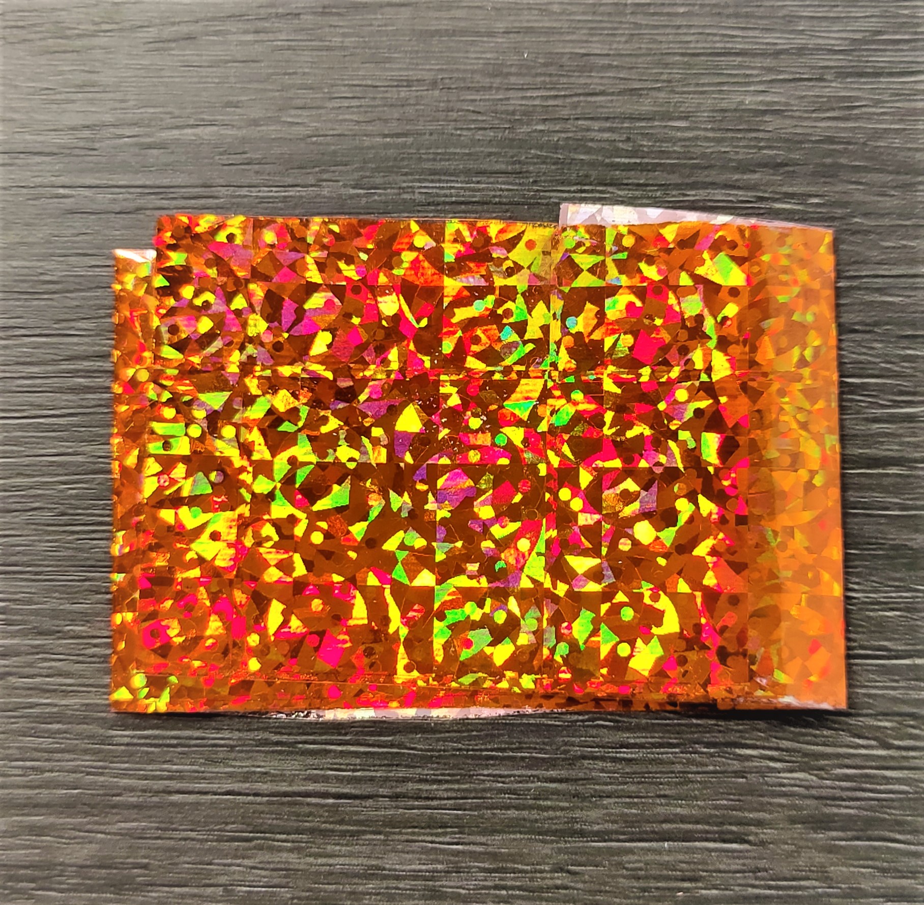 Folha holográfica laranja refletiva sobre superfície de madeira escura