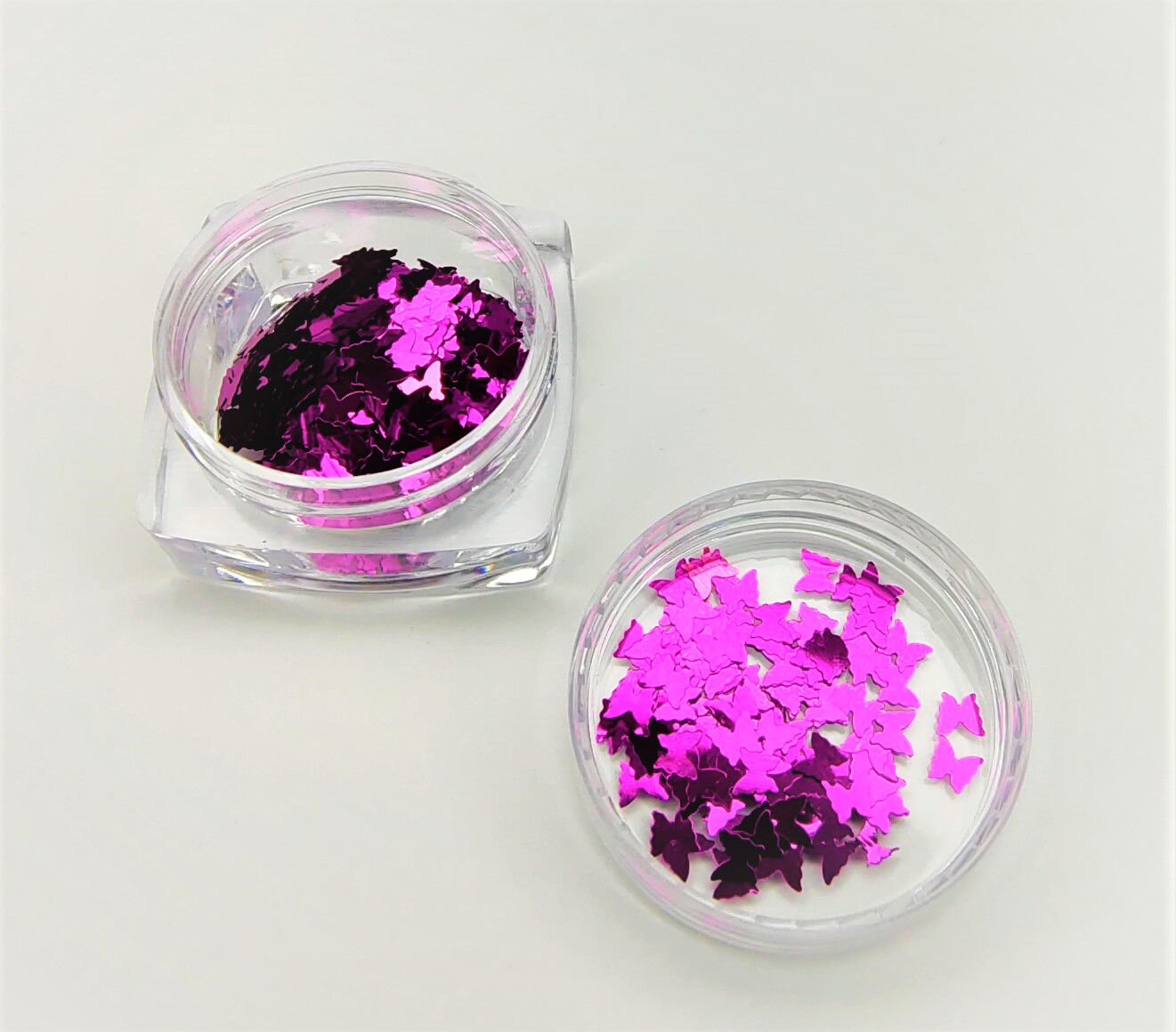 Dois frascos pequenos com glitter rosa em formato de morcegos sobre fundo branco