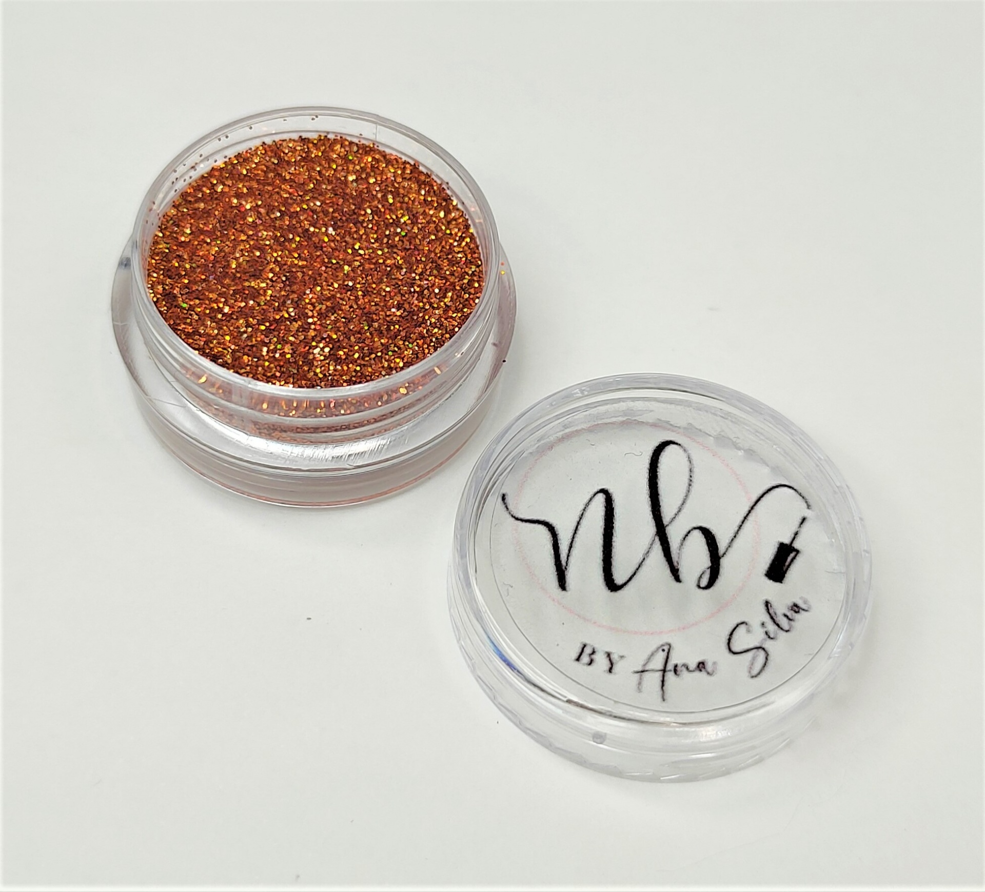 Pó brilhante laranja metálico em embalagem pequena redonda transparente com tampa texto 'nb BY Ana Silva'