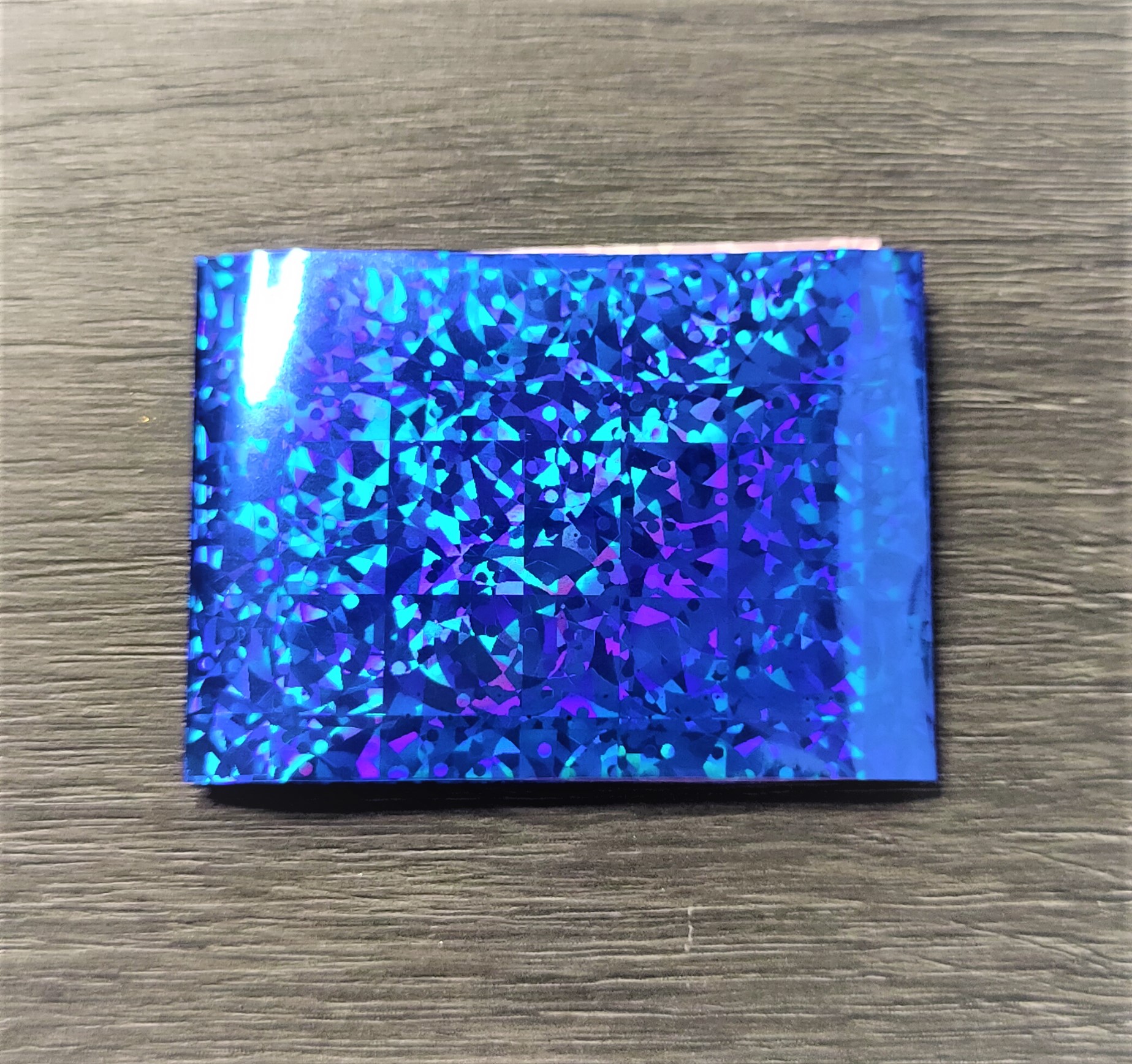 Folha holográfica retangular azul e roxa sobre madeira cinzenta