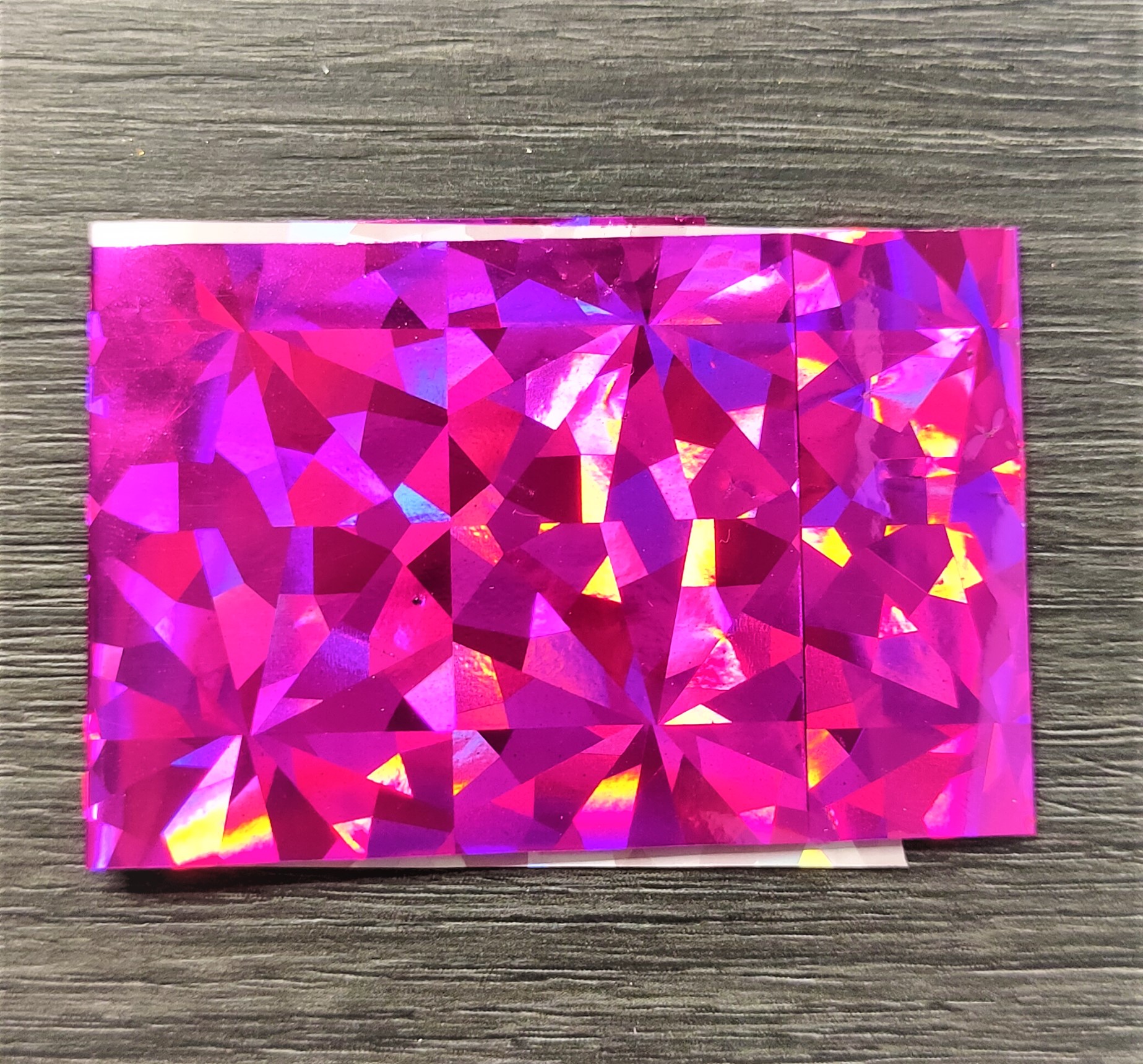 Papel holográfico rosa com padrão facetado sobre madeira cinzenta
