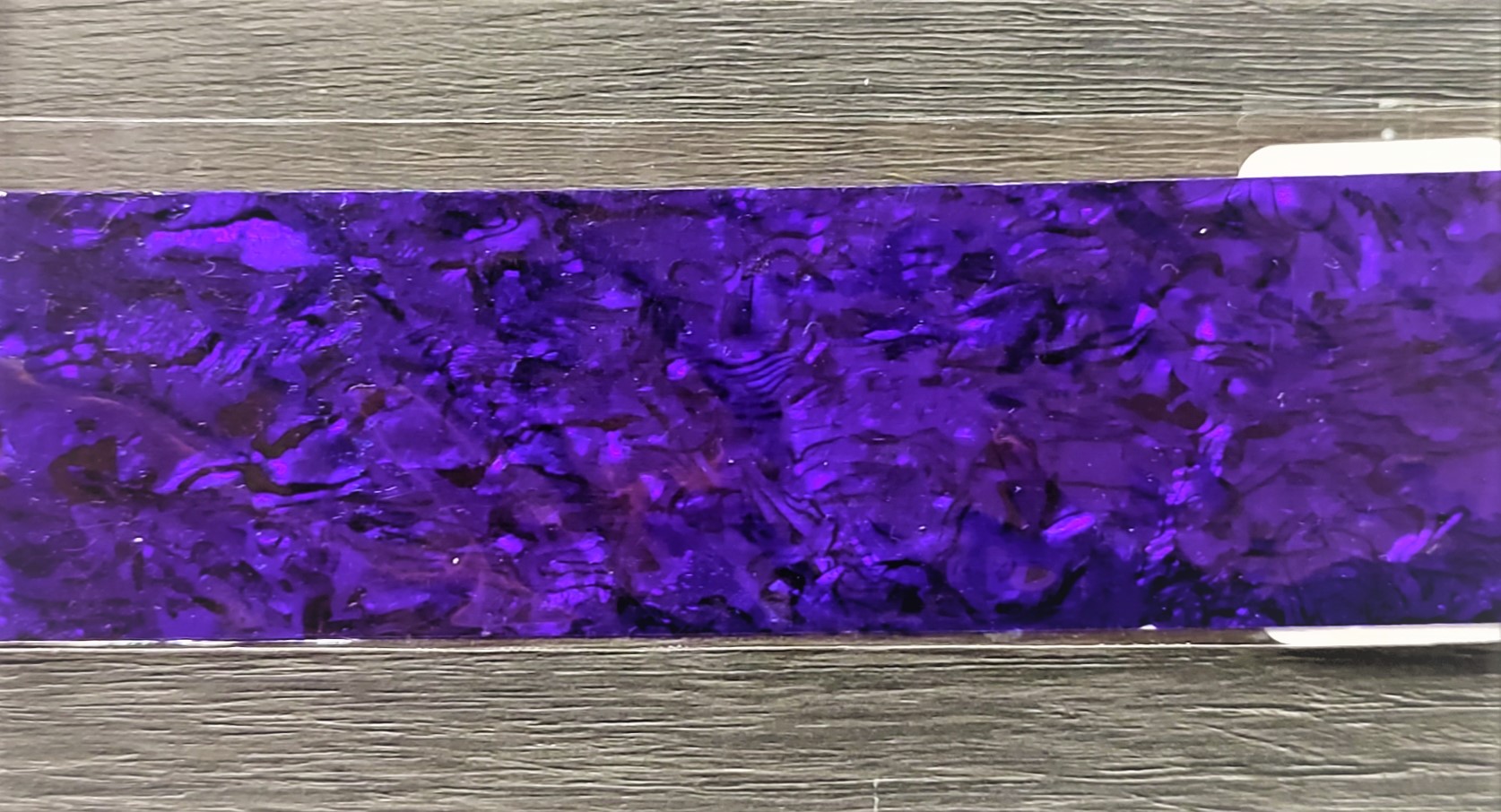 Placa retangular com padrão marmoreado roxo sobre superfície de madeira cinzenta