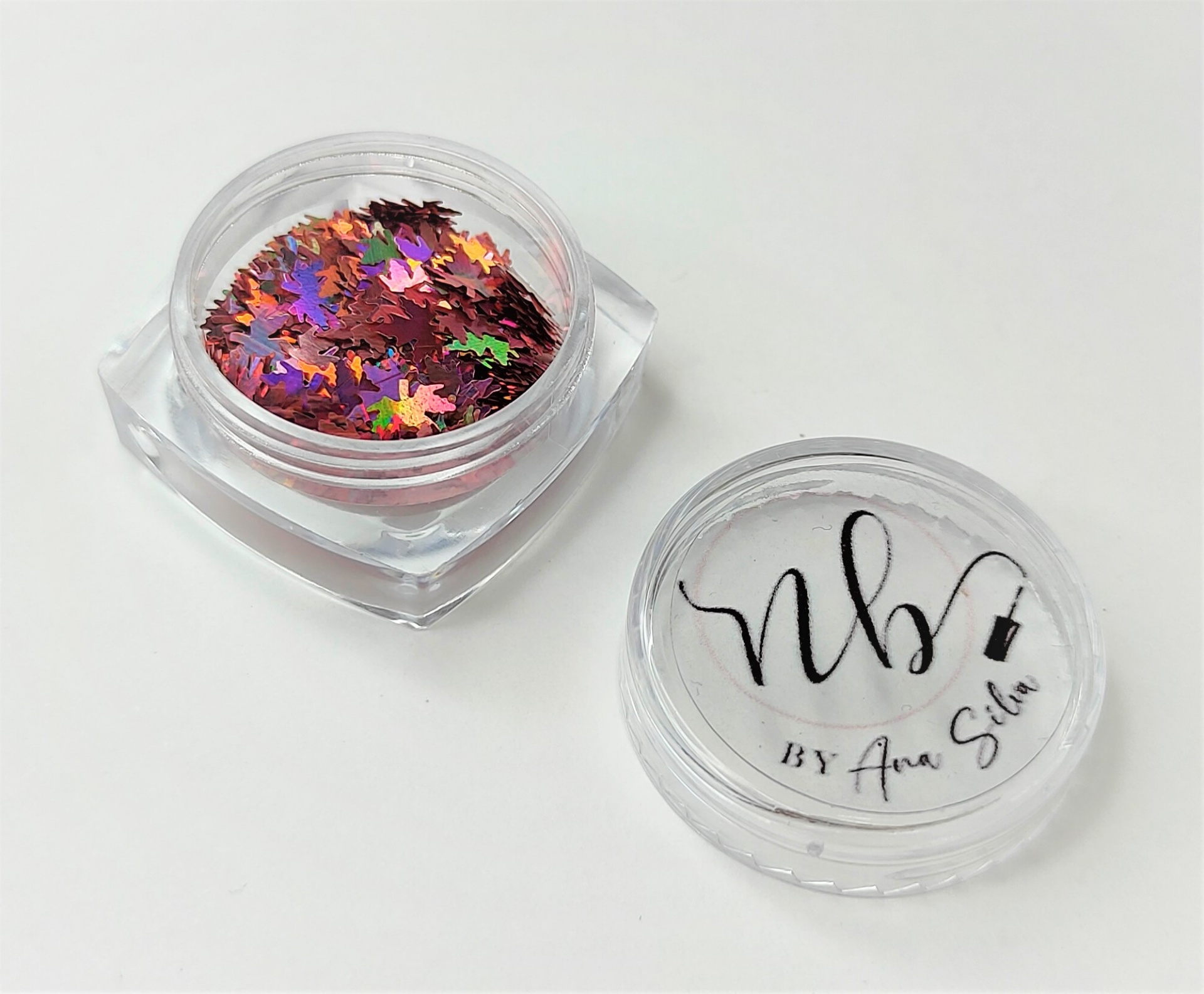 Frasco pequeno com purpurinas em forma de folhas coloridas e tampa com logo NB BY Ana Sílvia